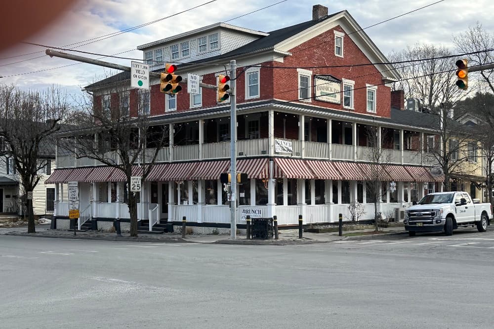 A historic red brick inn with a porch and striped awnings at a traffic intersection.
