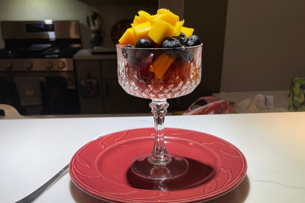 A crystal dish filled with mango and blueberries sits on a red plate.