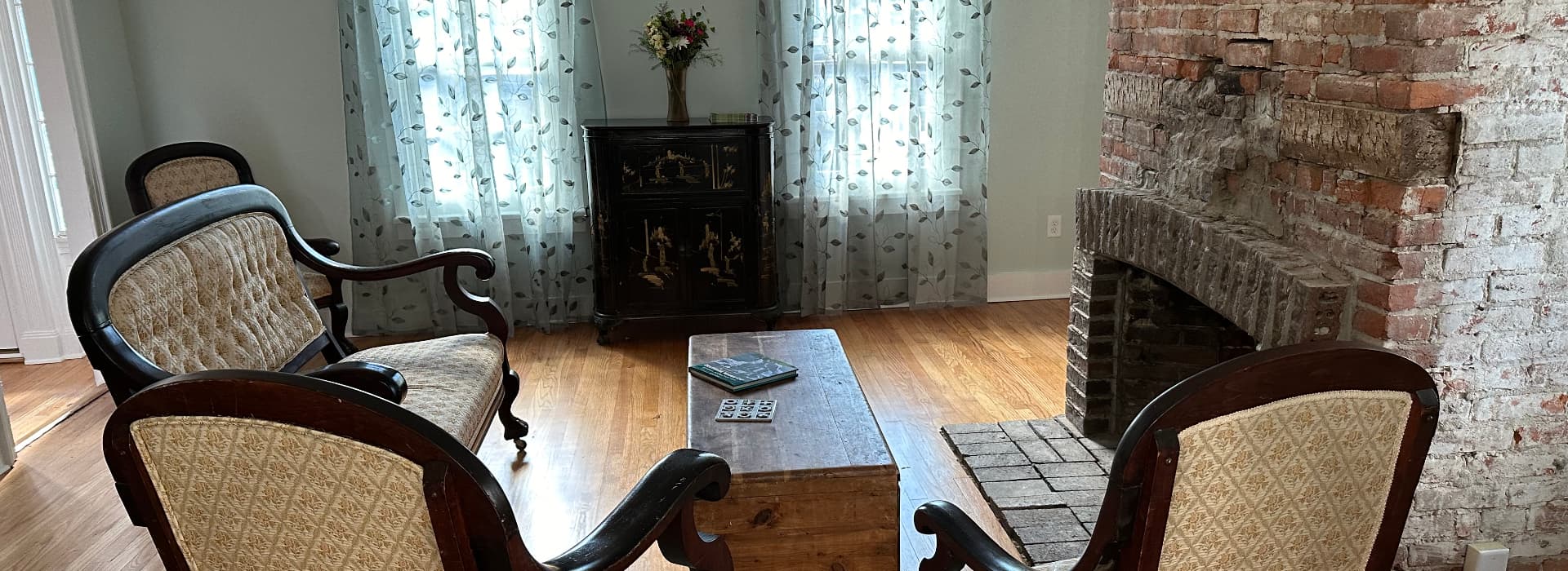 A cozy sitting area with vintage chairs, a wooden coffee table, and a fireplace against a brick wall.