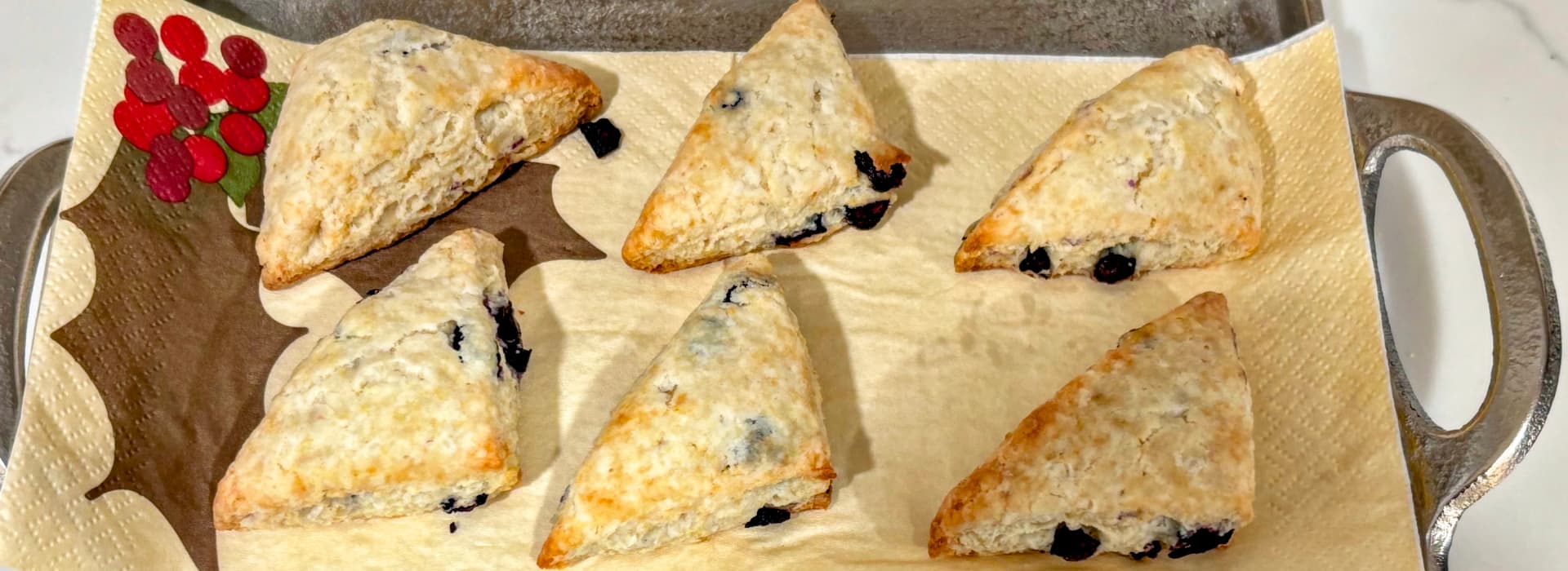 A tray of six triangular blueberry scones on a decorative paper napkin.