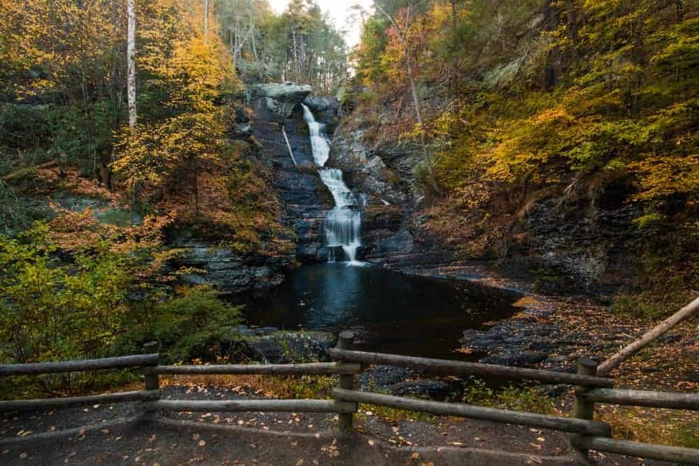 A tranquil waterfall cascades down rocky cliffs surrounded by vibrant autumn foliage.