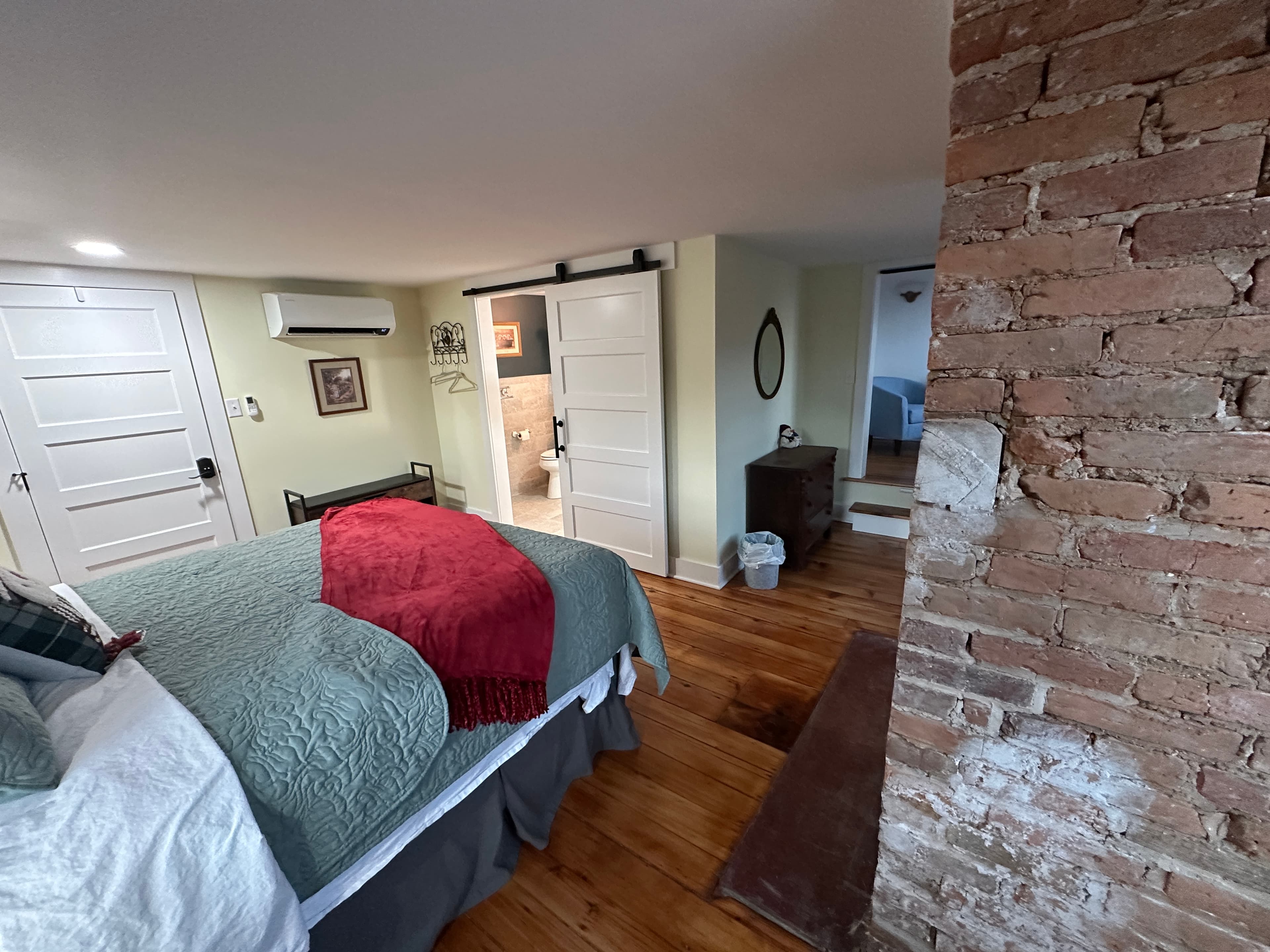 Spacious and cozy guestroom with queen bed, original hardwood floors, and sliding barn door leading to bathroom