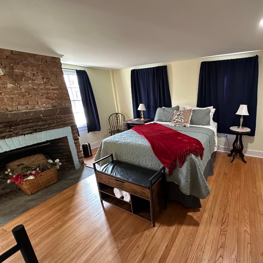 Cozy bedroom featuring a bed with a red throw, wooden furnishings, and a rustic brick fireplace.
