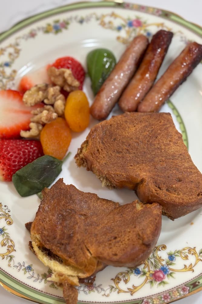 A plate with sliced bread, sausage links, strawberries, apricots, walnuts, and green jelly.
