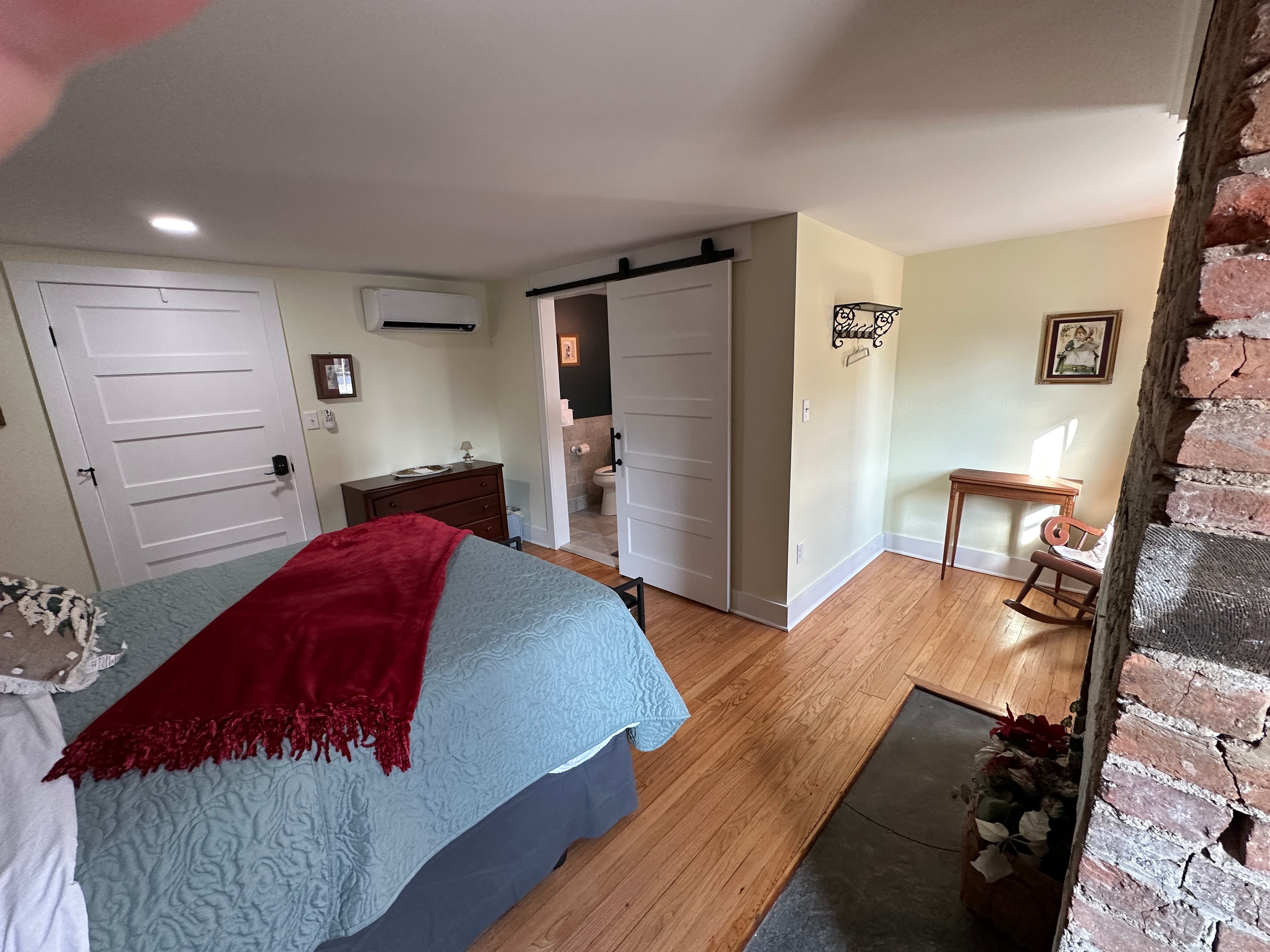 Guest room featuring a queen bed with blue and red bedding, a sliding barn door to the bathroom, and hardwood floors