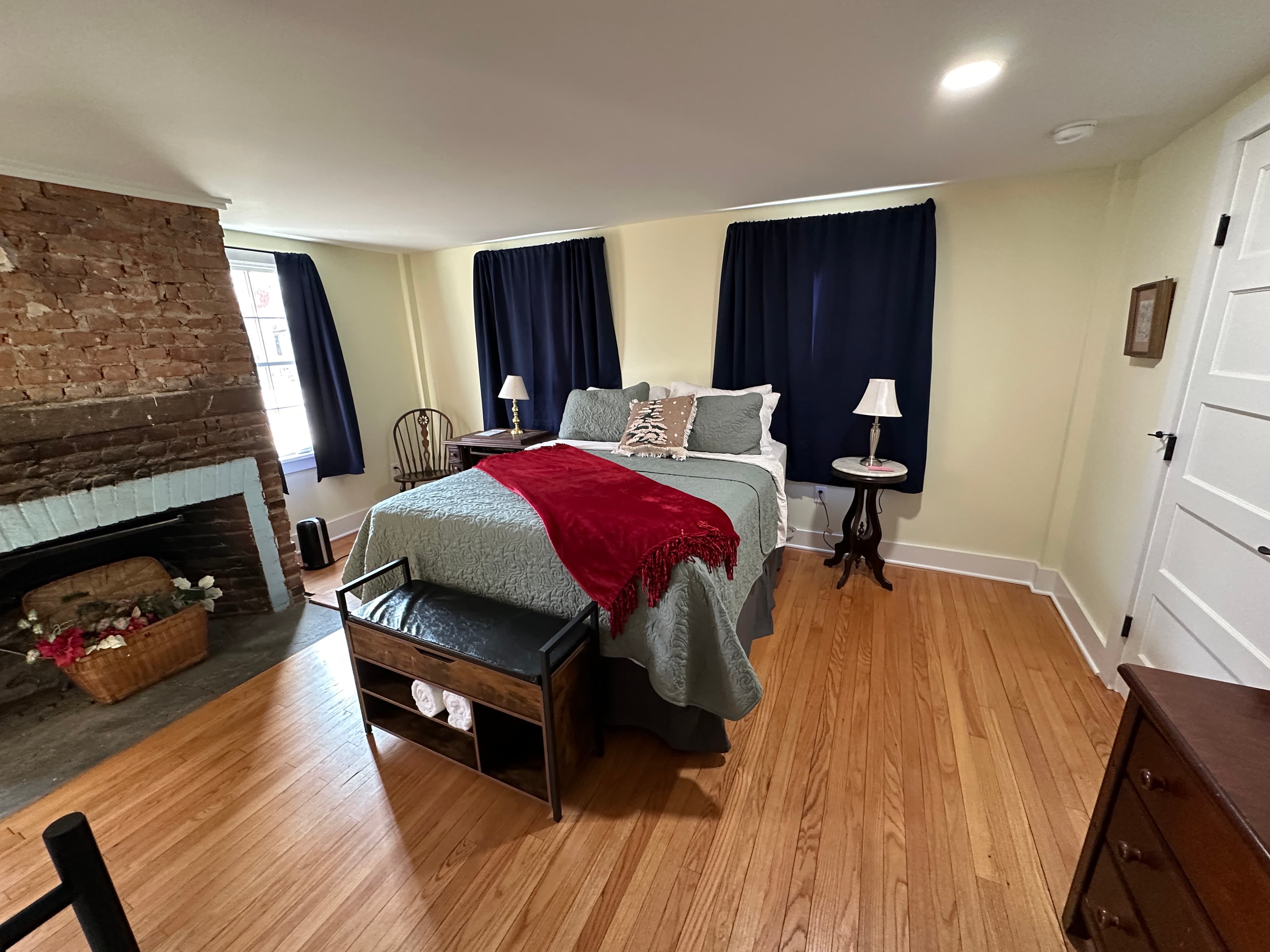 Spacious room featuring a queen bed with blue and red bedding, a stone fireplace, and hardwood floors