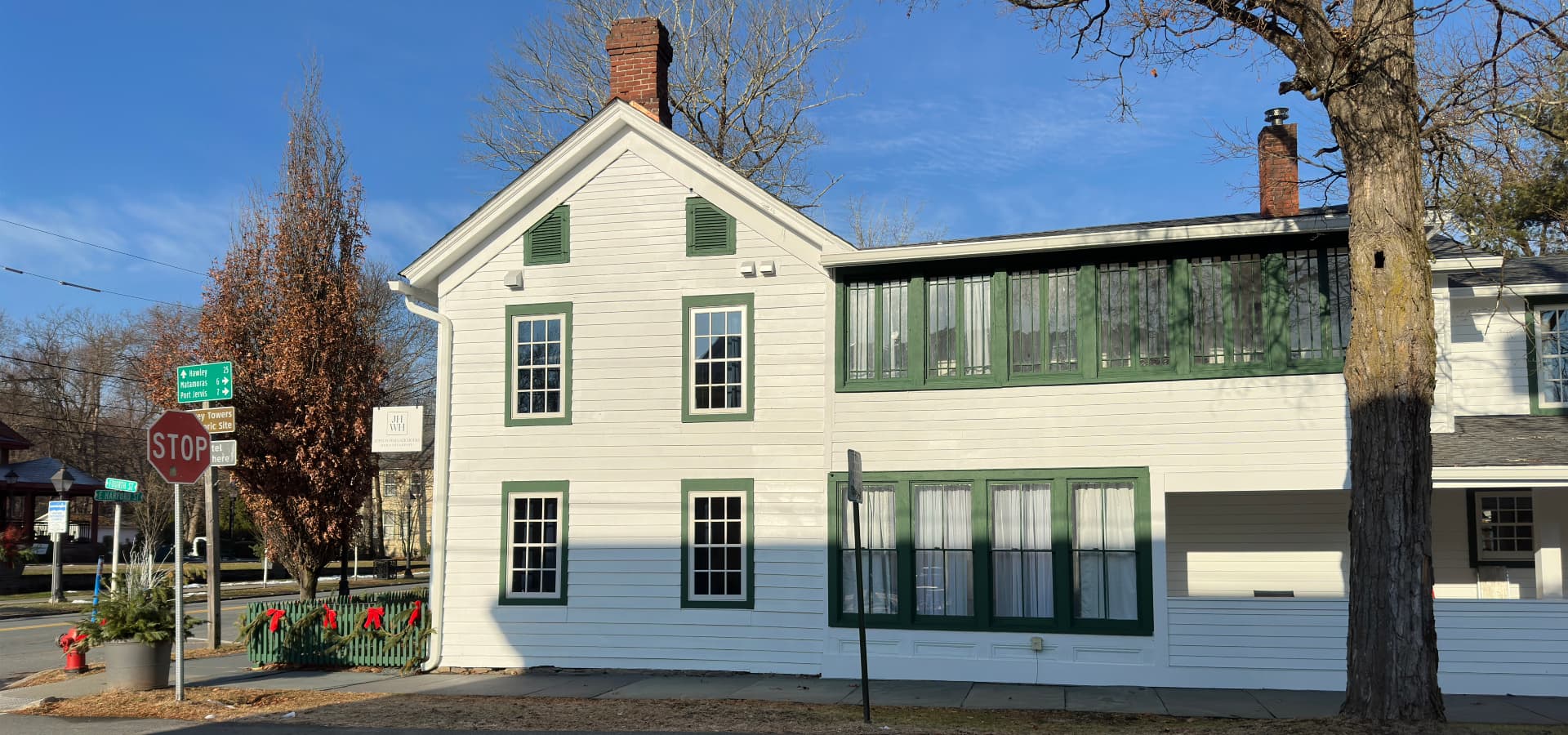 A white house with green accents and large windows is situated near a stop sign and directional signs in a suburban area.