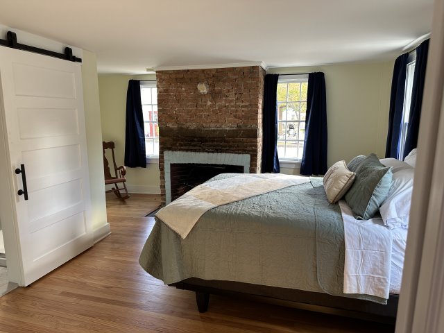 Bed on wood floors in the foreground with a rustic brick fireplace in the background.