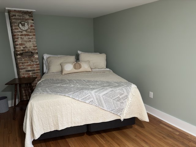 Bedroom with bed on wood floors with rustic brick chimney in the background.