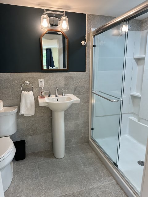 Bathroom with grey tile and white shower on the right with glass door.