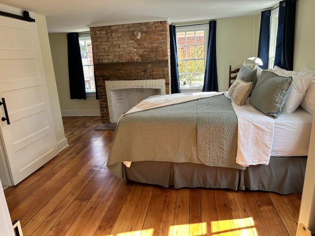 Bed on wood floors in the foreground with a rustic brick fireplace in the background.