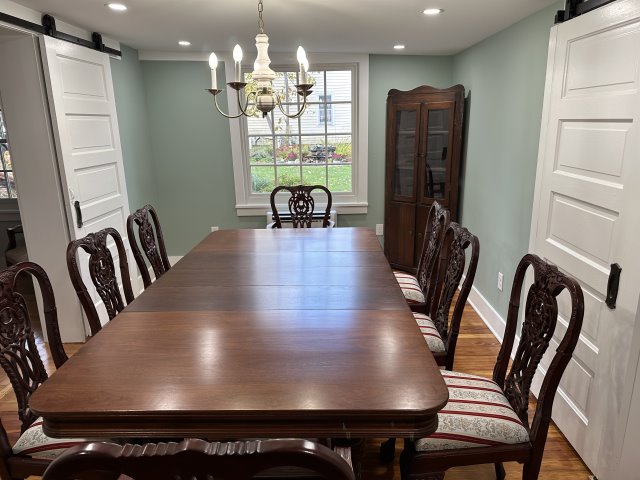 Large wooden dining room table on top of hardwood floors with chair around it.