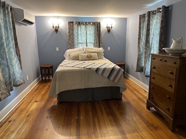 Bedroom with bed in the background on wood floors with dresser on the right.