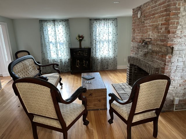 Living room with chairs on wood floors with rustic brick fireplace on right.